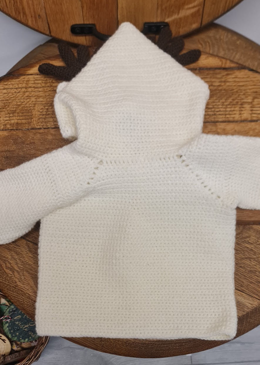 White knitted sweater on a wooden stool with a person's foot in black shoes in the background.